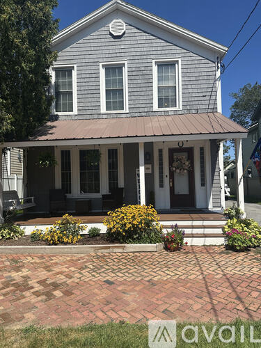 A grey house with a porch and a brick walkway in front.