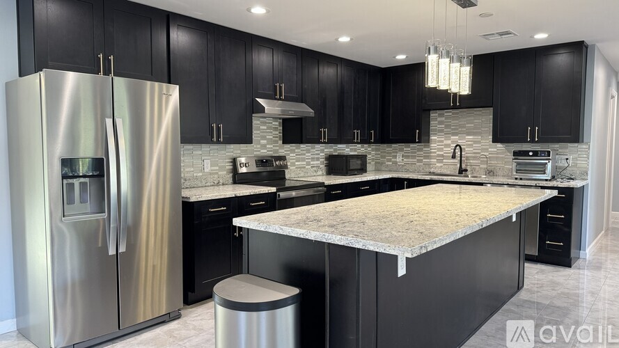 A modern kitchen with black cabinets and a stainless steel refrigerator.
