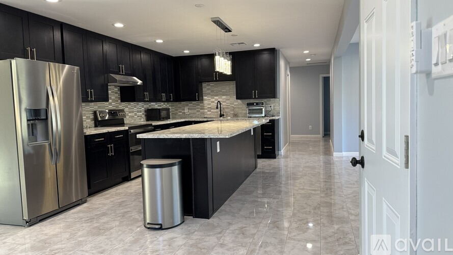 A modern kitchen with black cabinets and a stainless steel refrigerator.