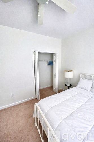 A white bed with a white mattress and a white pillow is in a room with a white ceiling fan.