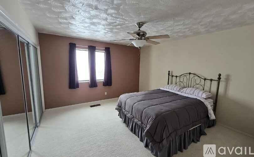 A bedroom with a bed, a ceiling fan, and a window with curtains.