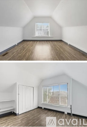 A room with wooden floors and white walls, with a window showing a view of buildings outside.