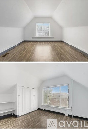 A room with wooden floors and white walls, with a window showing a view of buildings outside.
