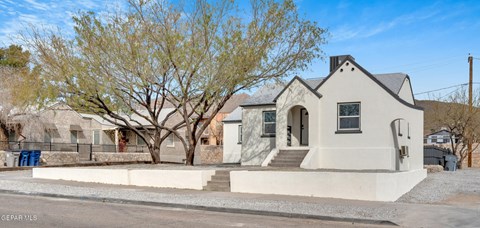 A small white house with a black roof and a tree in front.