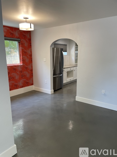 A spacious room with a red wallpapered wall and a white archway leading to another room.