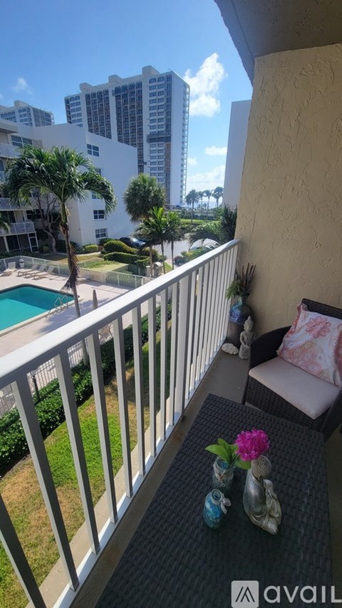 A balcony with a table and chairs overlooking a pool and buildings.