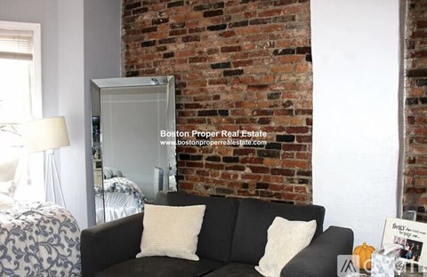 A living room with a black couch and a brick wall.