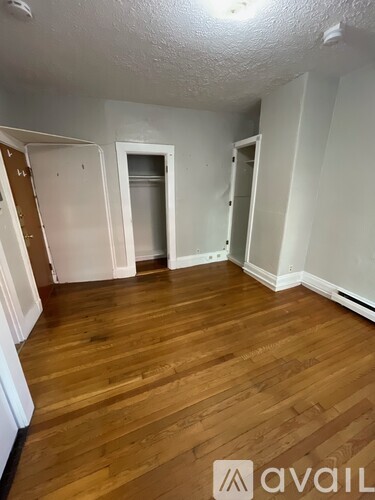 A room with wooden floors and white walls, with a door on the left and two open doors on the right.