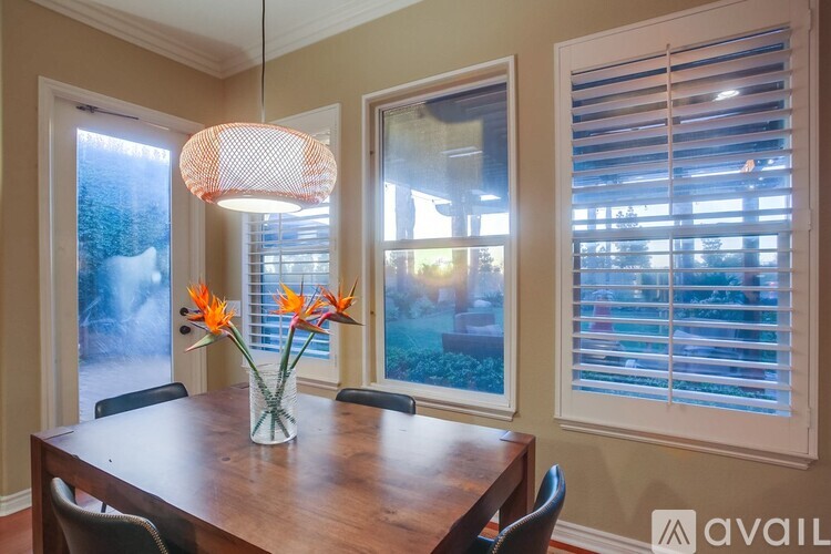A dining room with a wooden table and chairs, a vase with orange flowers, and a hanging light fixture.