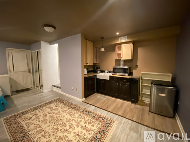 A room with a rug on the floor and a kitchen area with a sink and stove.