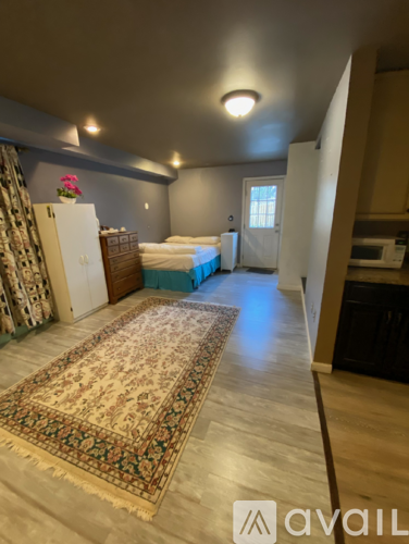 A room with a bed, a fridge, and a rug on the floor.