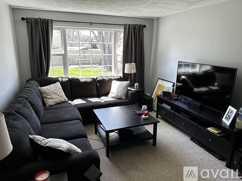 A black leather sofa with a grey cushion and a black coffee table in front of a television.