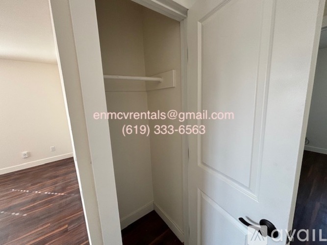 A white door with a black handle is open to a small, empty room with a wooden floor.