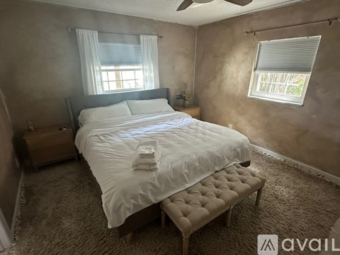 A bedroom with a bed, bench, and two windows.