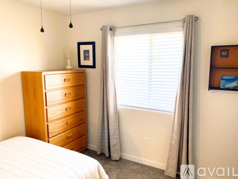 A bedroom with a bed, dresser, and window with curtains.