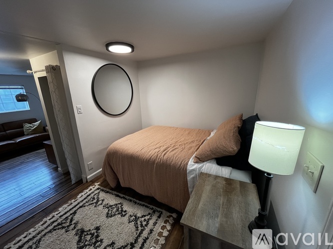 A bedroom with a bed, lamp, and a round mirror on the wall.