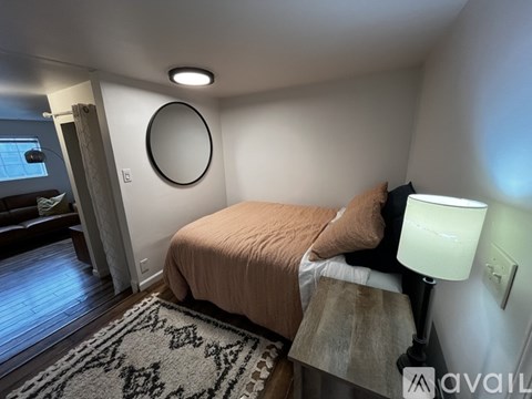 A bedroom with a bed, lamp, and a round mirror on the wall.