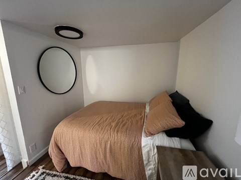 A bedroom with a bed, pillows, and a round mirror on the wall.