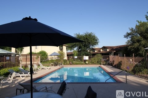 A pool with a black umbrella in the foreground and a house in the background.