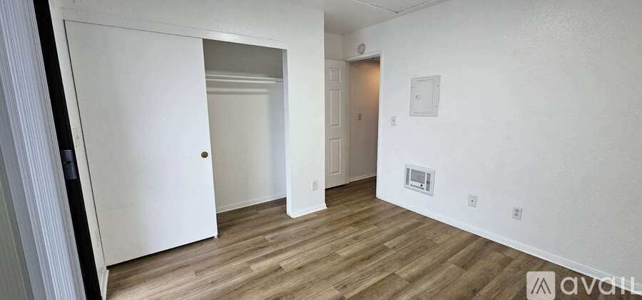 A room with wooden flooring and white walls, with a door on the left and a small window on the right.