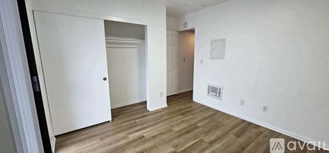 A room with wooden flooring and white walls, with a door on the left and a small window on the right.
