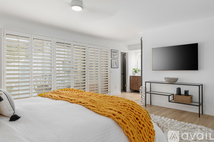 A bedroom with a bed covered in a yellow blanket and a flat screen TV mounted on the wall.