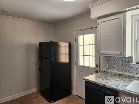A black refrigerator in a kitchen with a white door and a tiled backsplash.