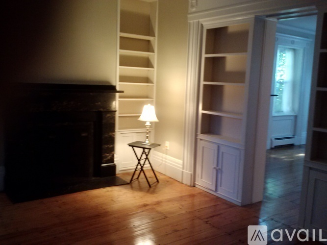 A lamp sits on a table in a room with a fireplace and wooden floors.
