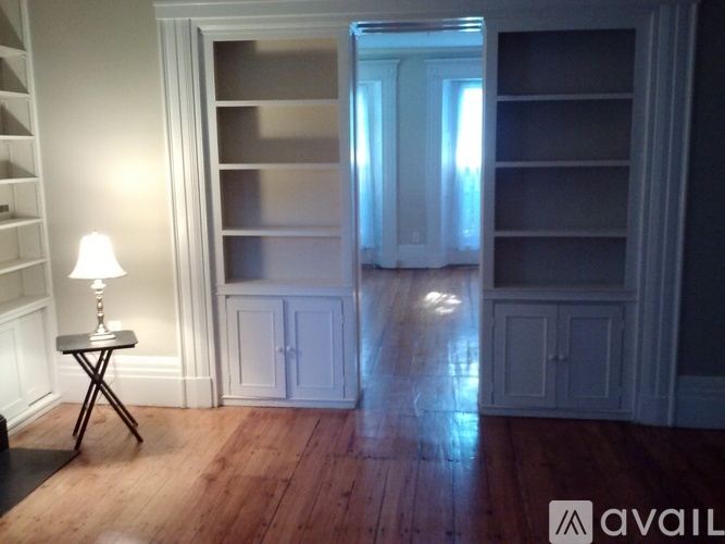 A lamp sits on a small table in a room with a wooden floor and white walls.
