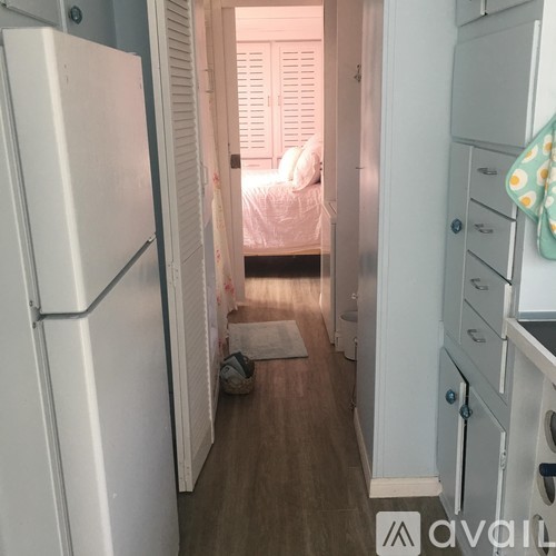 A white refrigerator is on the left side of a narrow hallway.