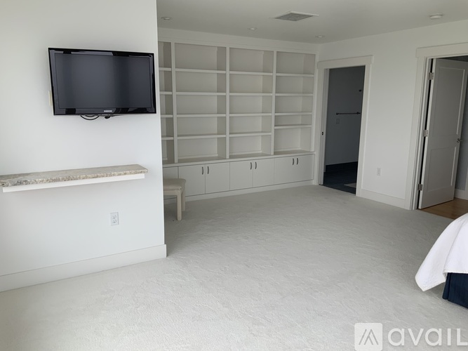 A living room with a flat screen TV mounted on the wall and a row of shelves.