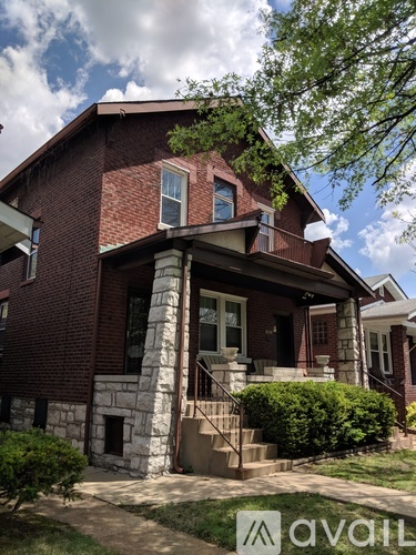 A red brick house with a porch and a tree in front.