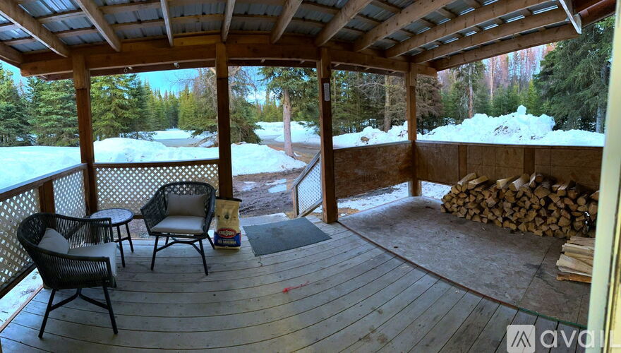 A wooden deck with chairs and a table is surrounded by snow.