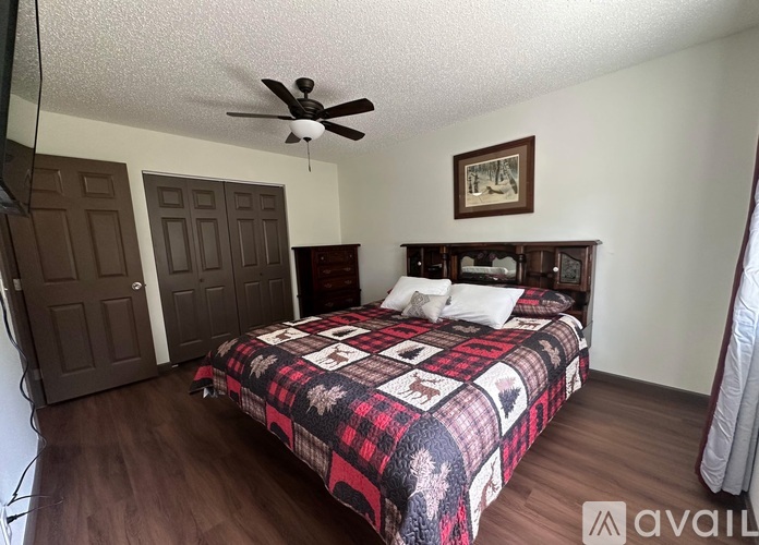 A bedroom with a bed, a ceiling fan, and a painting on the wall.