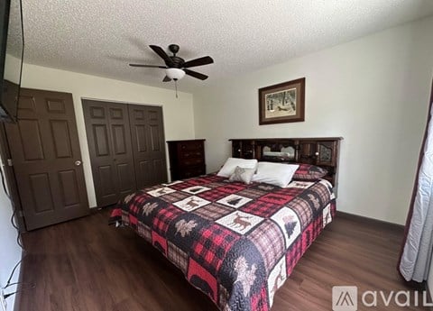 A bedroom with a bed, a ceiling fan, and a painting on the wall.