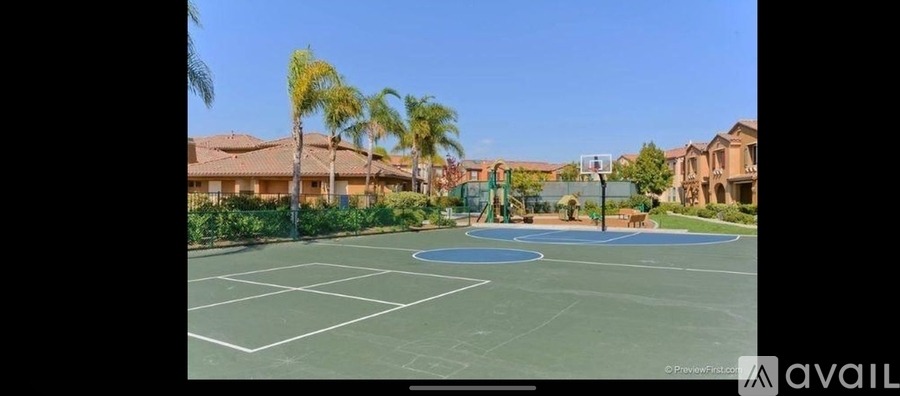 A tennis court surrounded by palm trees and residential buildings.