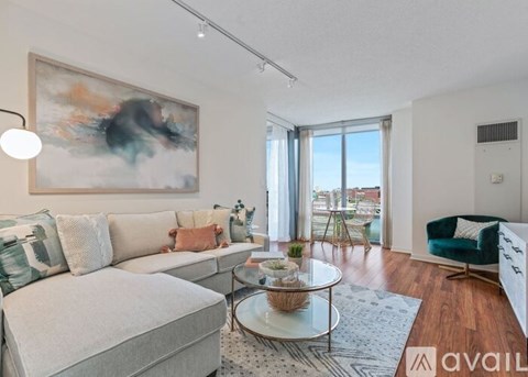 A living room with a grey sofa, a glass table, and a painting on the wall.