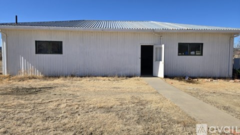 A white building with a corrugated metal roof and a door is surrounded by dry grass.