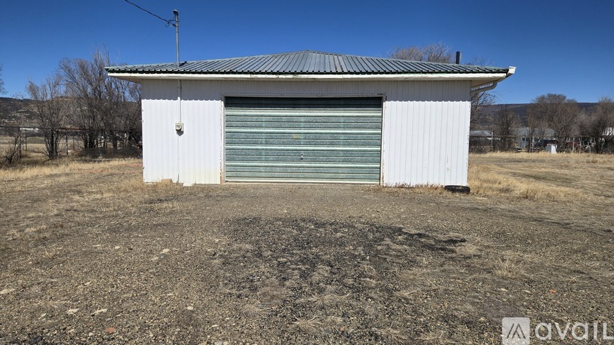 A small white building with a green roller shutter door sits in a field.