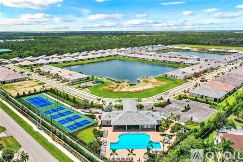 A bird's eye view of a community with a swimming pool, tennis courts, and a lake.
