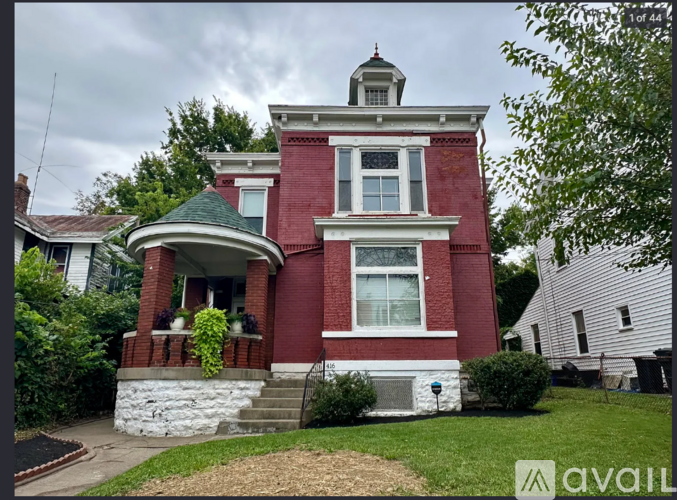 A red brick house with a green roof and a white house in the background.