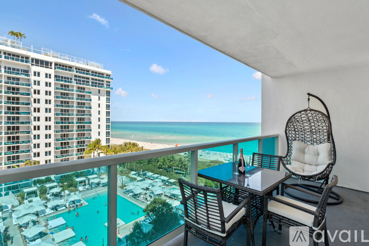 A balcony with a table and chairs overlooking a pool and beach.