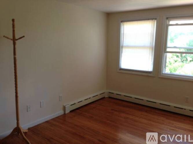 A room with a wooden floor, a window with blinds, and a wooden cross on the wall.