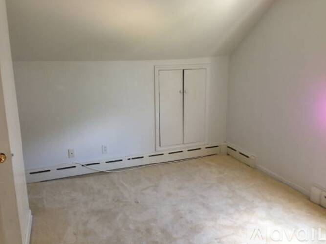 A white bedroom with a door and a wall socket.