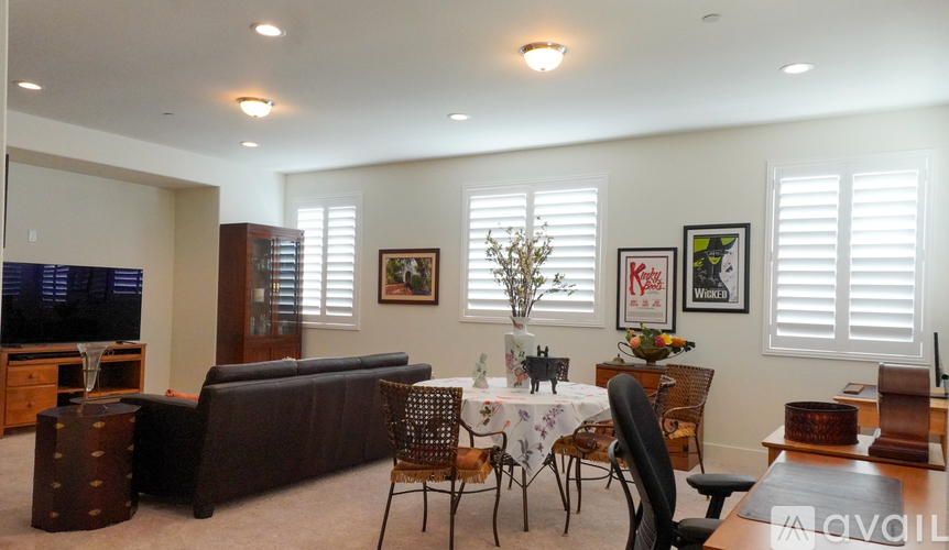 A living room with a brown couch, a dining table with chairs, and a television.