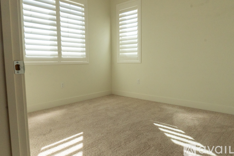 A room with white walls and a carpeted floor with sunlight coming through the blinds.