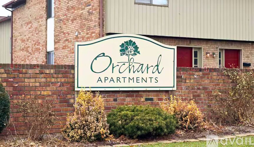 A sign for Orchard Apartments is displayed in front of a brick building.