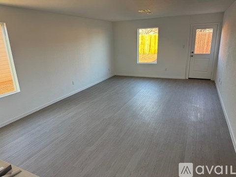 A spacious room with wooden flooring and two windows.