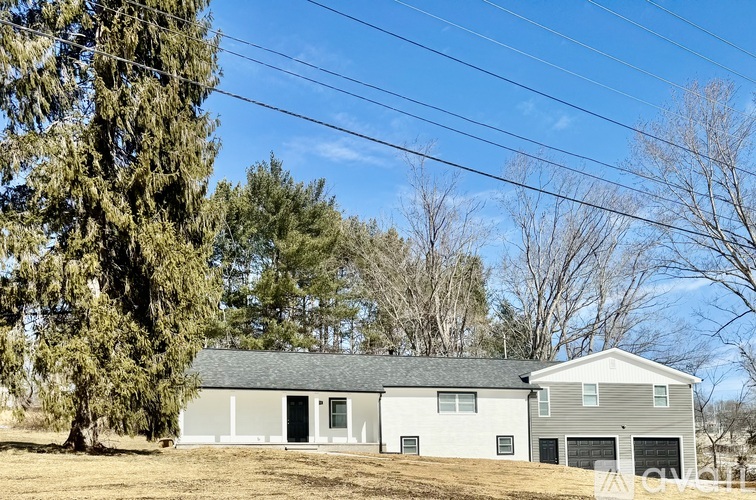 A house with a grey roof and white walls is surrounded by trees and has a clear blue sky above.