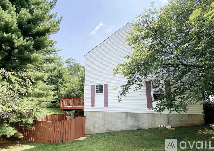 A house with a white siding and a red window is surrounded by trees.